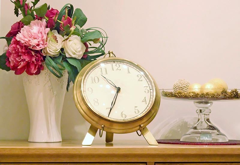A tabletop or mantel arrangement featuring a large, round brass or gold-colored vintage-style clock sitting on a wooden surface.